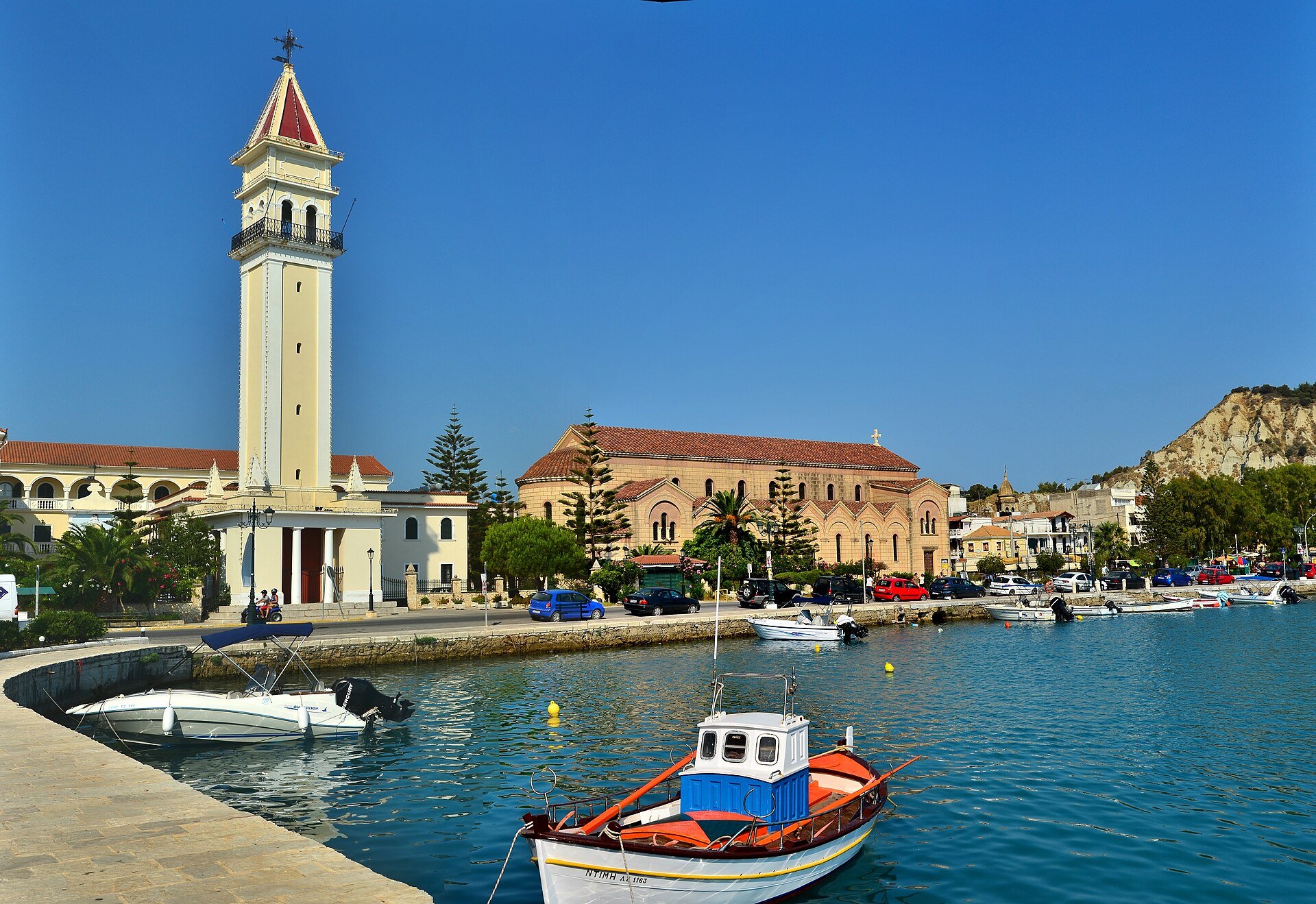 Glockenturm und Kirche des Agios Dionysios hinter dem Hafenbecken mit Fischerbooten