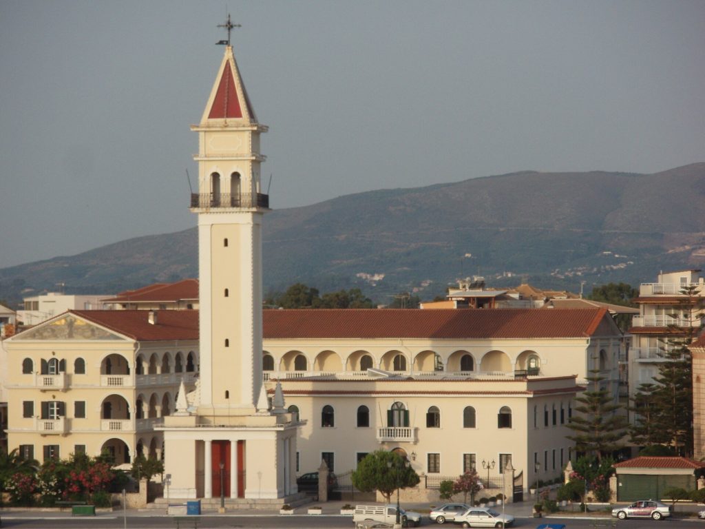 Hoher weißer Glockenturm mit roter Spitze vor dem Klostergebäude am Hafen von Zakynthos-Stadt
