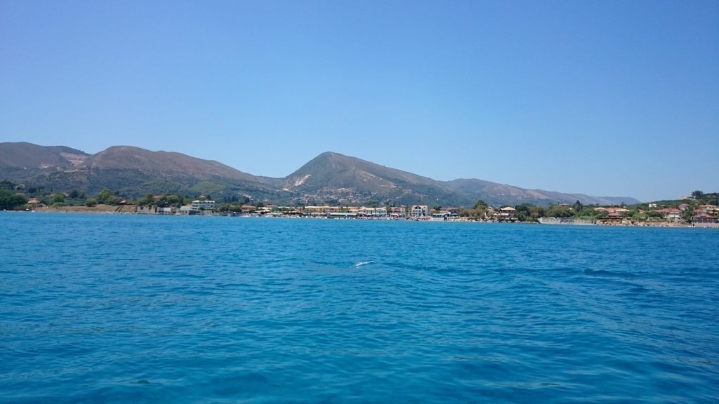 Küste bei Agios Sostis vom Meer aus gesehen, dahinter Berge