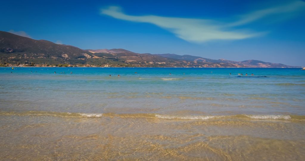 Flaches, klares Wasser am Sandstrand von Alykanas, im Hintergrund Hügel