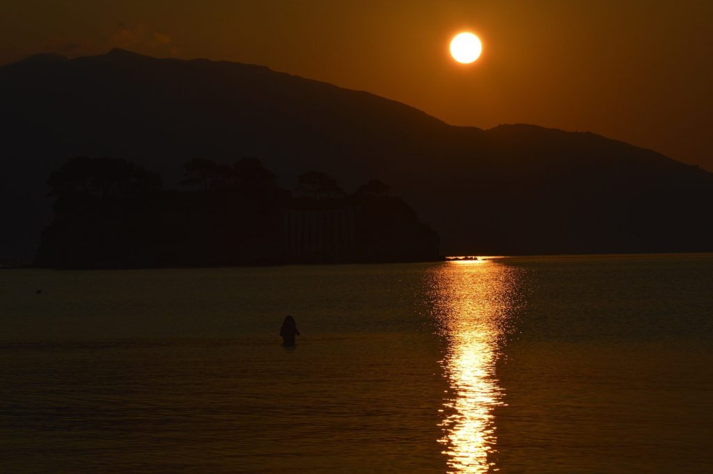 Die Sonne geht hinter einem Berg auf und spiegelt sich im Meer vor der Insel Agios Sostis
