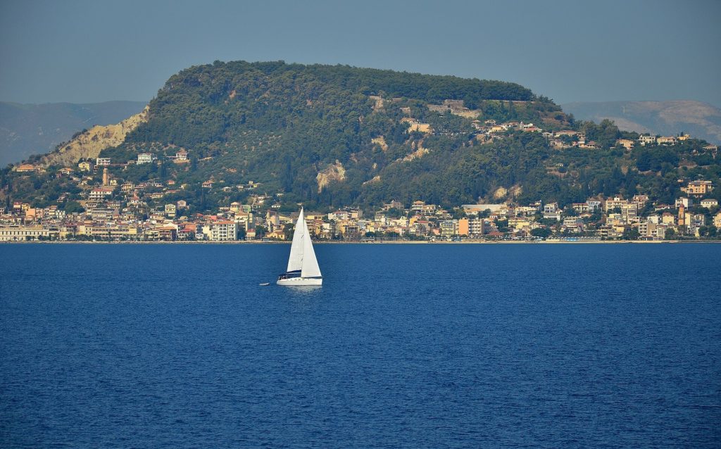 Bewaldeter Hügel von Bochali über der Uferzeile von Zakynthos-Stadt, davor ein Segelboot auf dem Meer