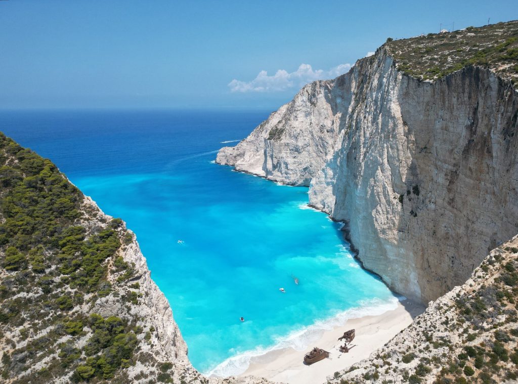 Blick von den Klippen hinunter in die Navagio-Bucht mit weißem Strand, Schiffswrack und türkisfarbenem Wasser
