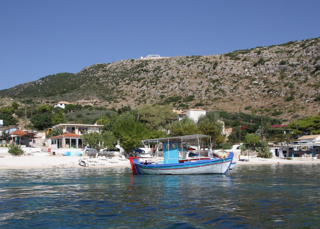 Bunt bemaltes Fischerboot vor einem kleinen Sandstrand mit Häusern in Agios Nikolaos