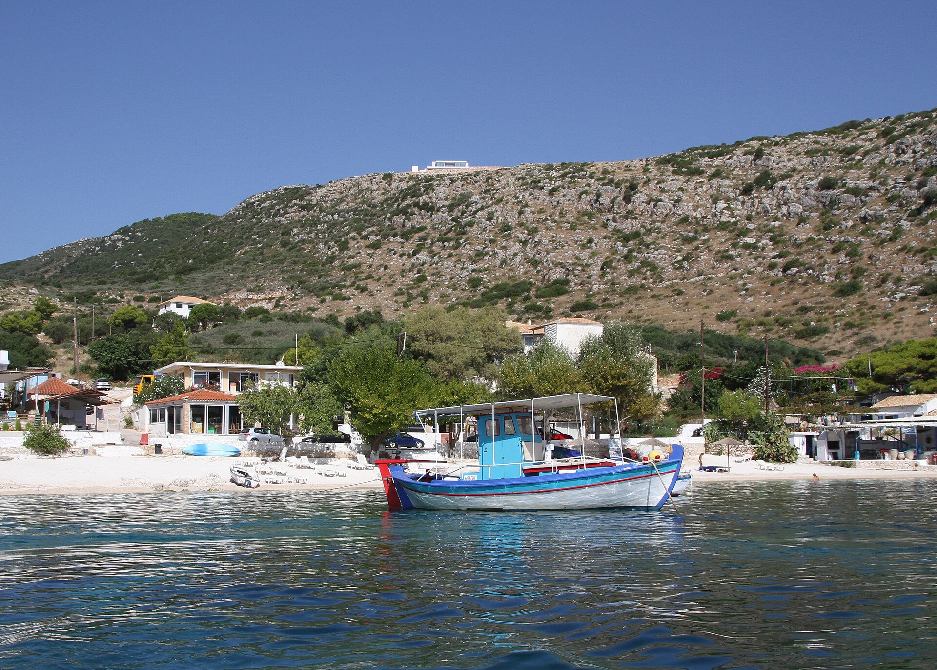 Bunt bemaltes Fischerboot vor einem kleinen Sandstrand mit Häusern in Agios Nikolaos