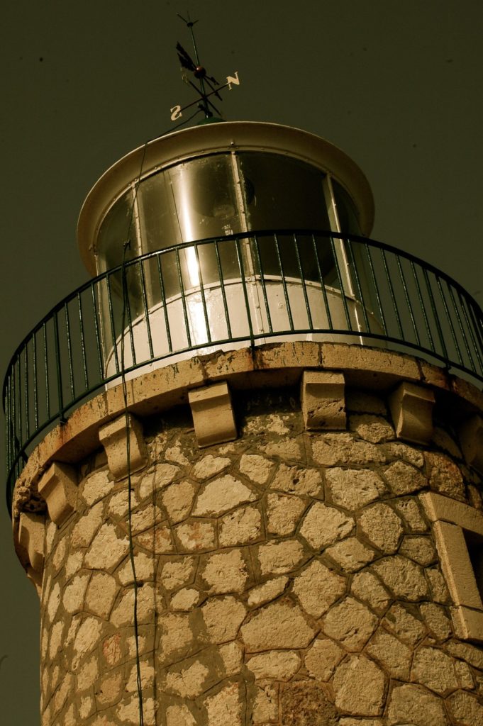 Runder Leuchtturm aus Bruchstein mit Galerie und Laterne vor dunklem Himmel