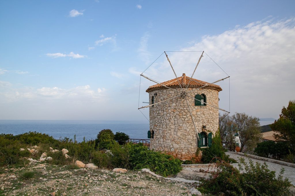 Runde Windmühle aus Naturstein mit Ziegeldach und Flügelgerüst, dahinter das Meer
