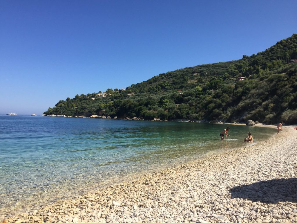 Kiesstrand mit klarem Wasser unter einem bewaldeten Hang