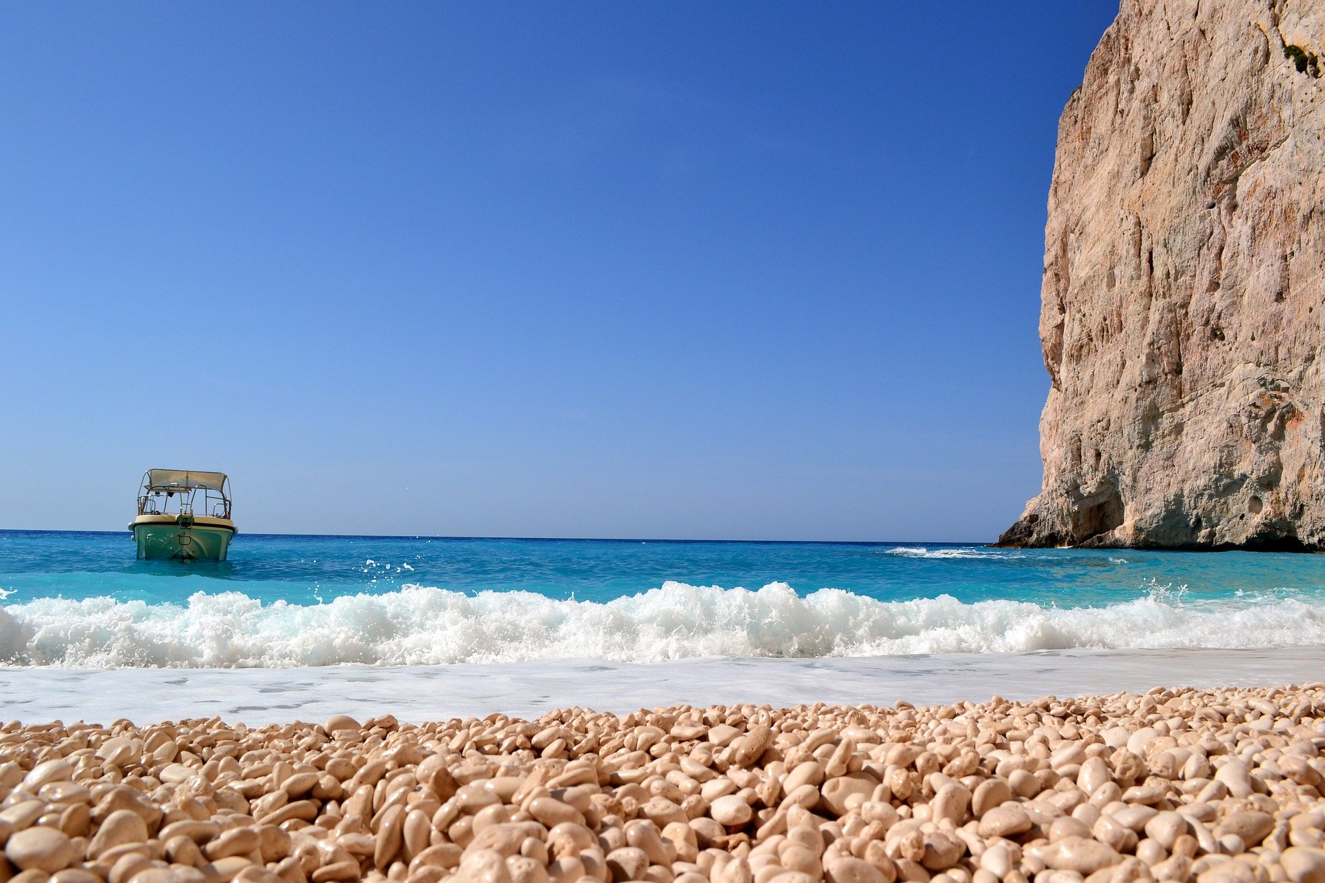 Kiesstrand mit Brandung, ein Ausflugsboot und eine helle Felswand