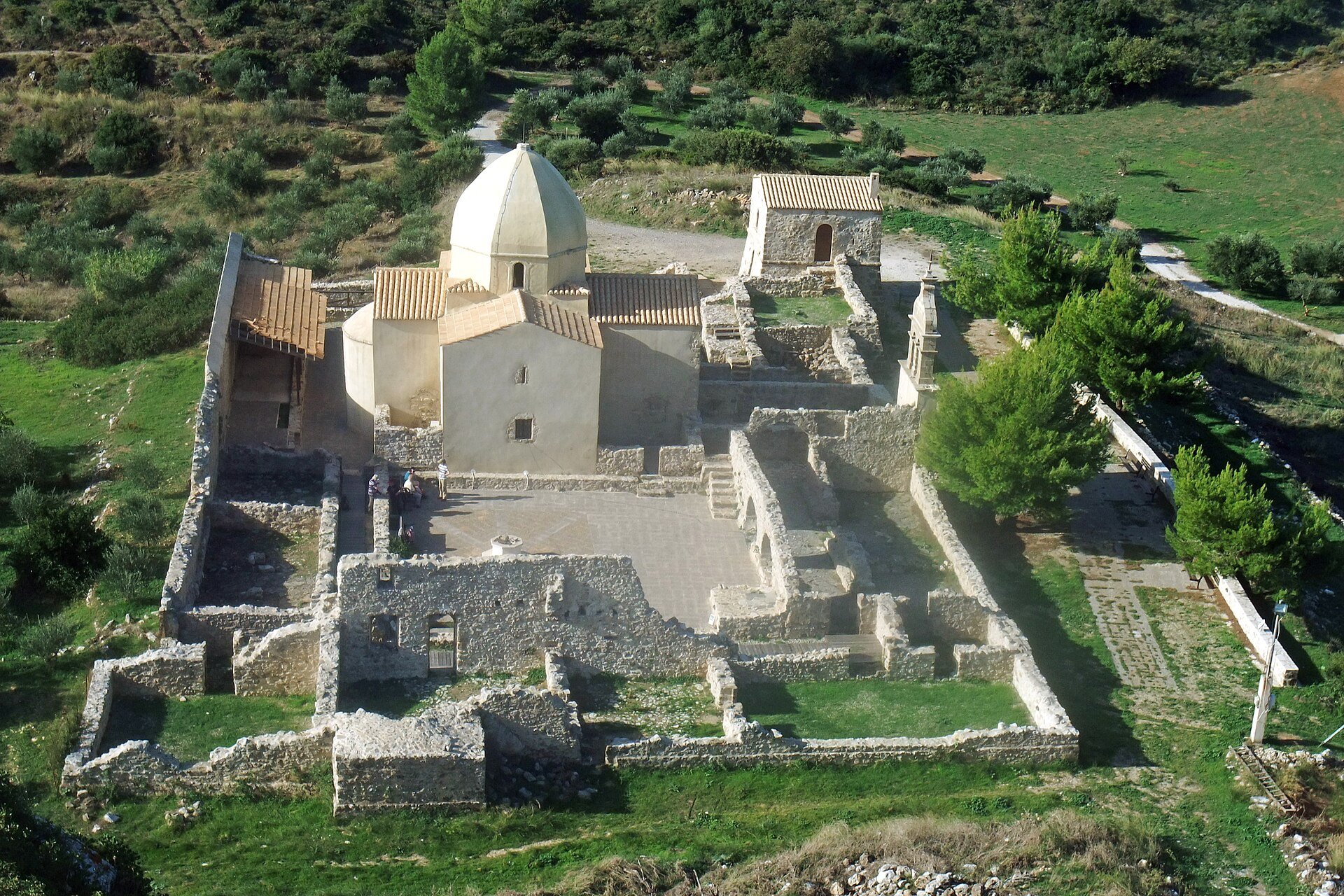 Kirche mit Kuppel inmitten von Klosterruinen auf einem grünen Berghang