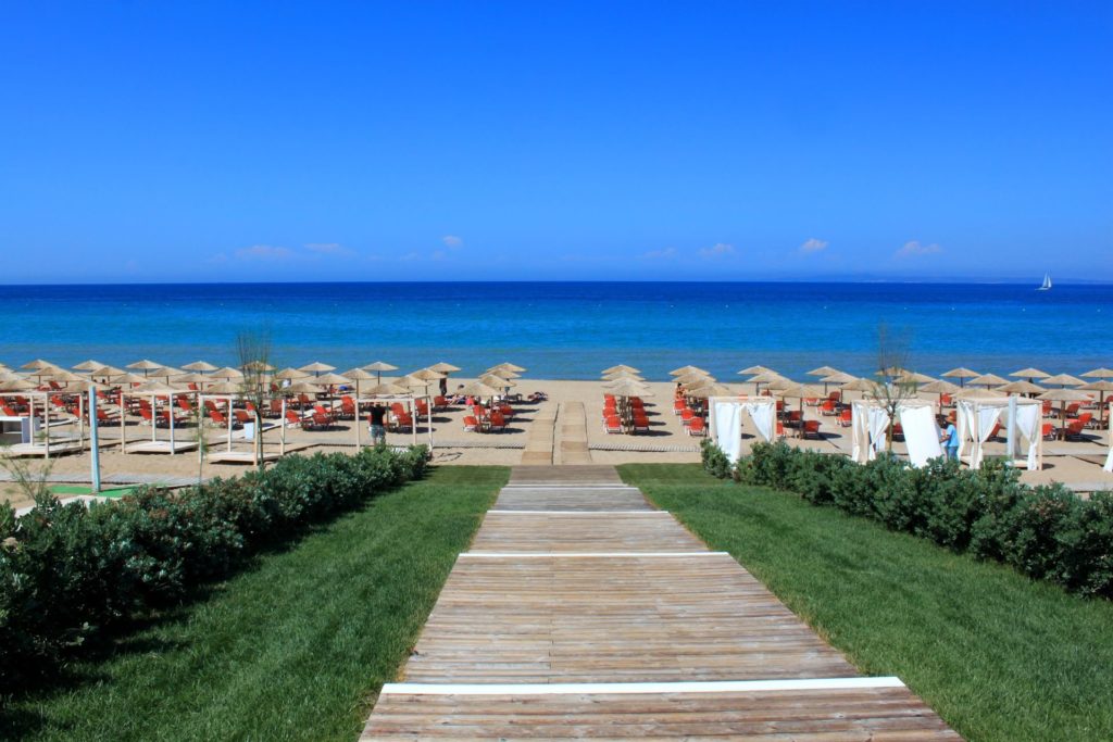 Reihen von Strandliegen mit Schirmen an einem Sandstrand auf Zakynthos, dahinter das Meer