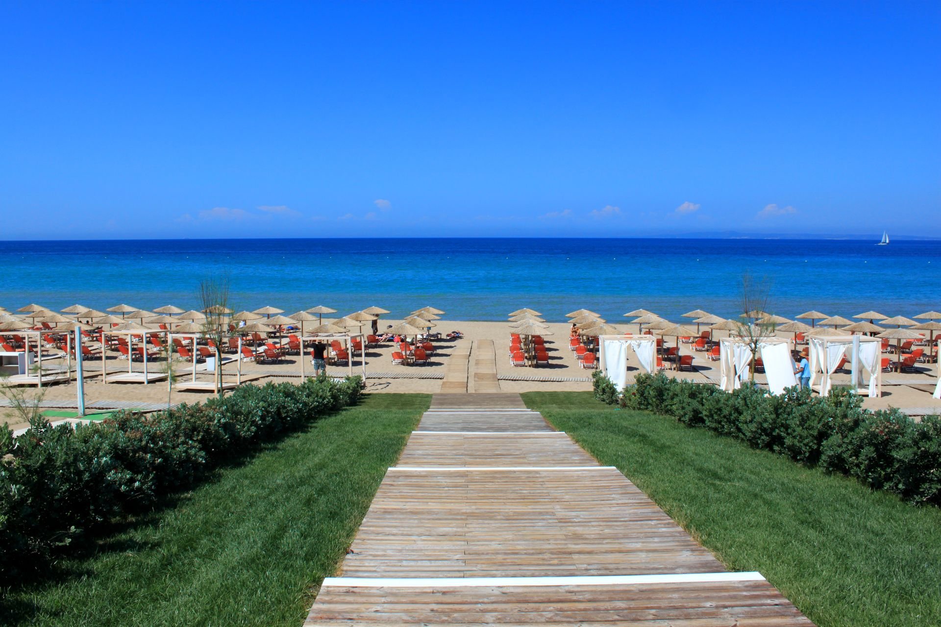 Reihen von Strandliegen mit Schirmen an einem Sandstrand auf Zakynthos, dahinter das Meer