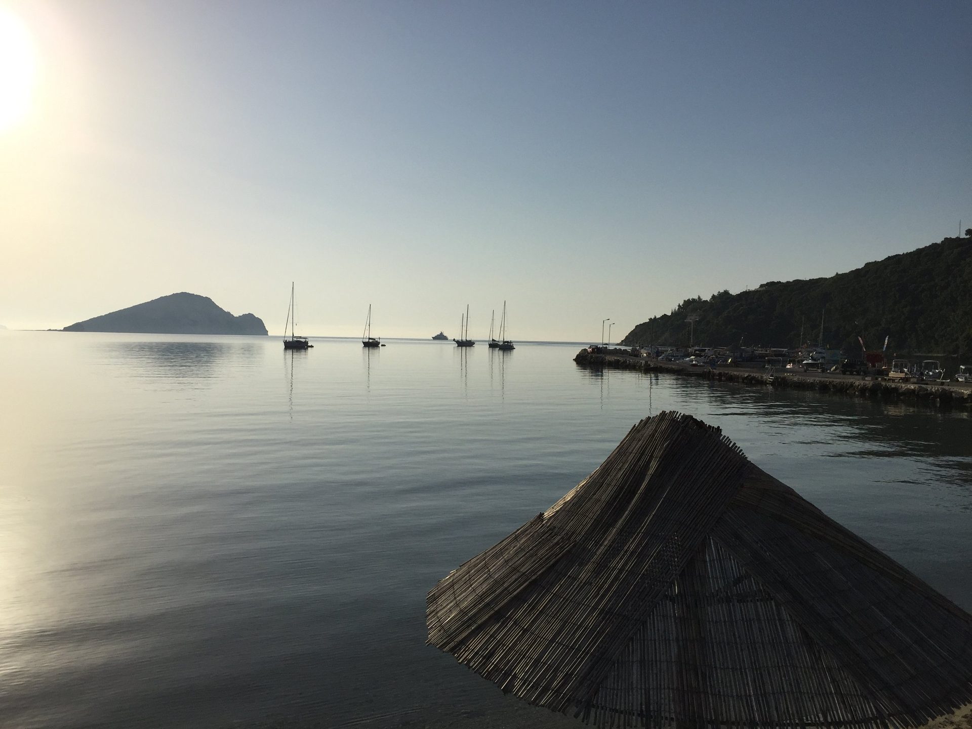 Strohschirm im ruhigen Wasser am Morgen, im Hintergrund Marathonisi