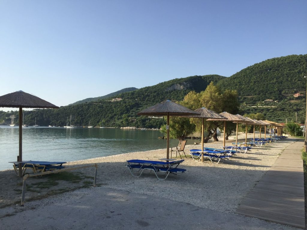 Strandliegen und Schirme am Strand von Limni Keri, dahinter die bewaldeten Hänge