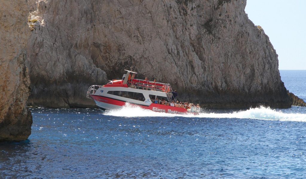 Rot-weißes Ausflugsboot fährt vor einer hohen Felswand durchs Meer