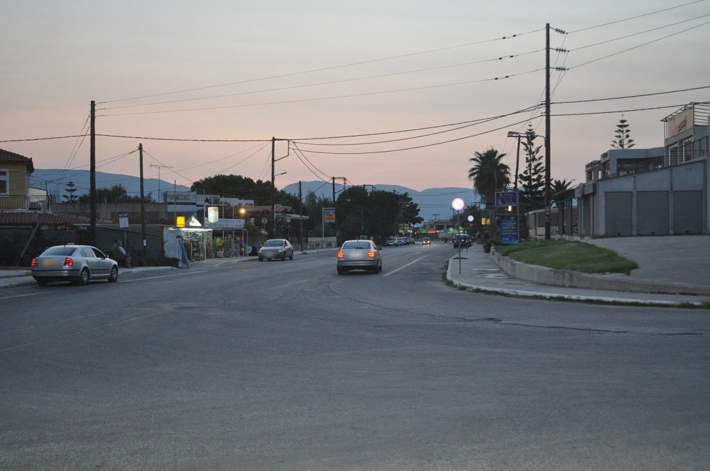 Hauptstraße von Kalamaki in der Abenddämmerung mit Läden und Autos