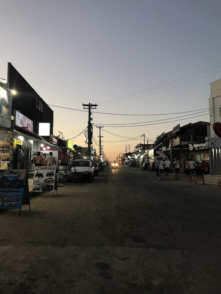Hauptstraße von Laganas in der Abenddämmerung mit beleuchteten Geschäften und Bars