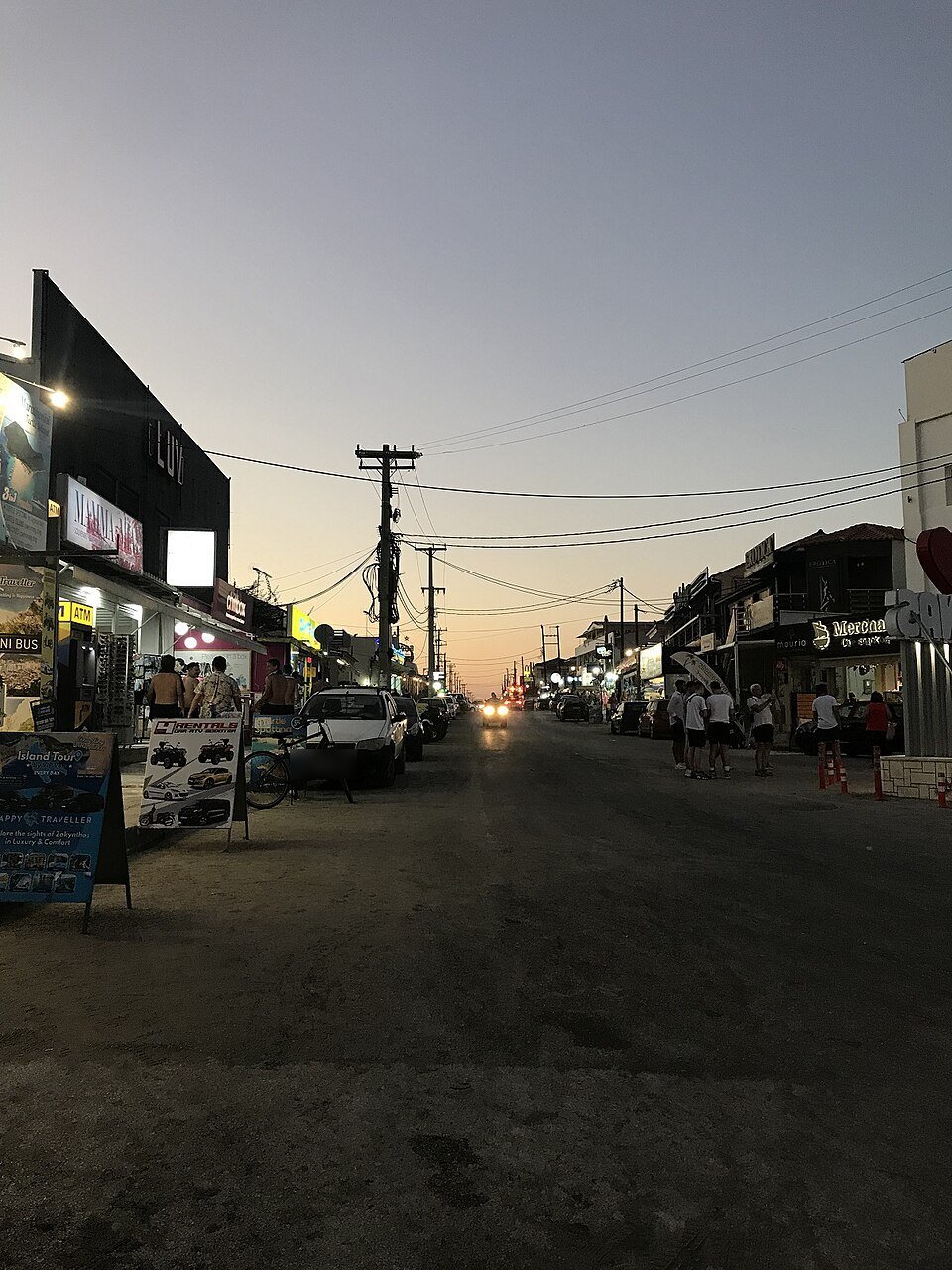Hauptstraße von Laganas in der Abenddämmerung mit beleuchteten Geschäften und Bars