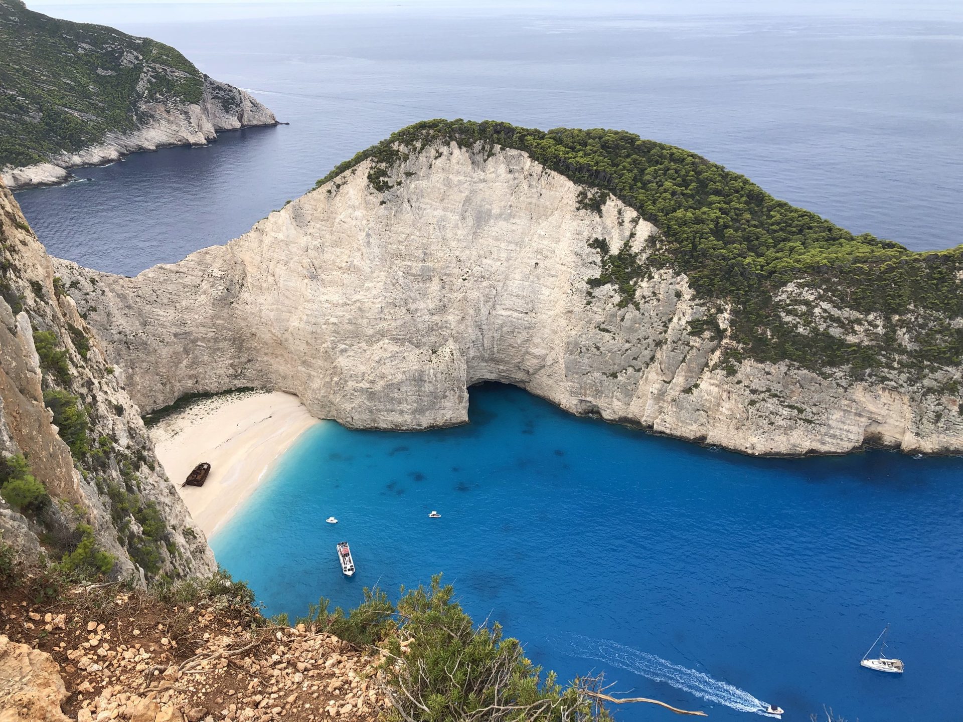 Blick von der Klippe auf die Bucht von Navagio mit Strand, Wrack und Booten