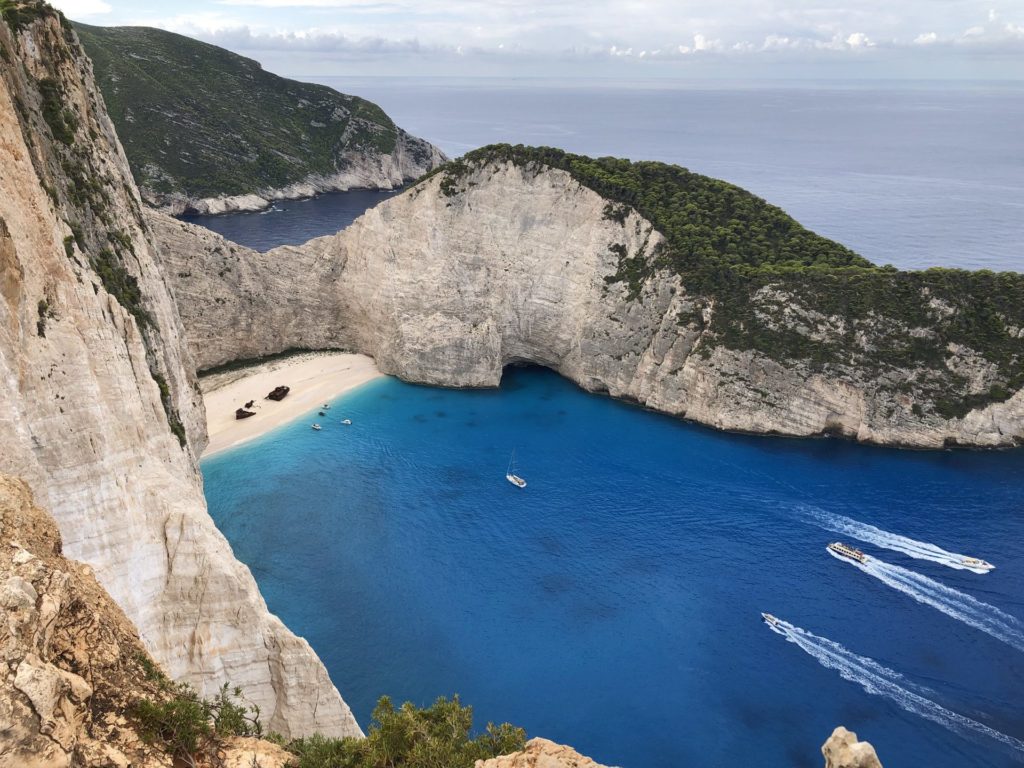 Die senkrechte Felswand über der Bucht von Navagio, unten Boote im türkisen Wasser