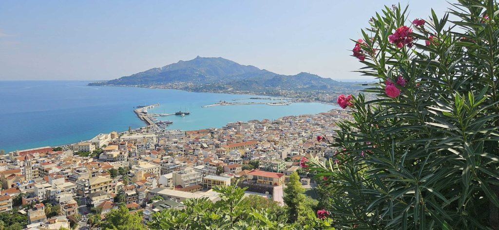 Blick über Zakynthos-Stadt mit Hafenmole, dahinter der Berg Skopos, rechts blühender Oleander