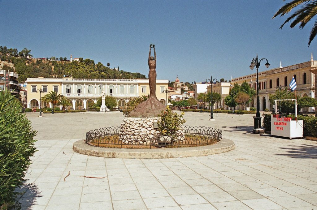 Freiheitsstatue in der Mitte des Solomos-Platzes, dahinter Gebäude mit Arkaden