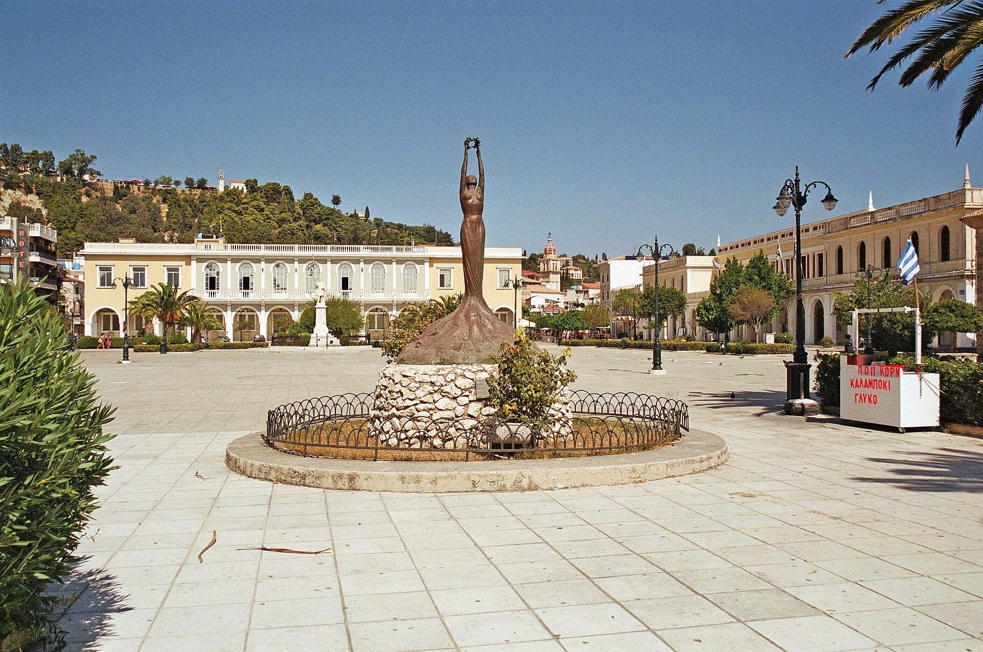 Freiheitsstatue in der Mitte des Solomos-Platzes, dahinter Gebäude mit Arkaden