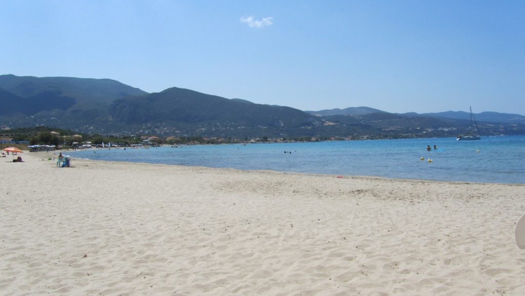 Breiter heller Sandstrand an der Bucht von Alykes mit Bergen im Hintergrund
