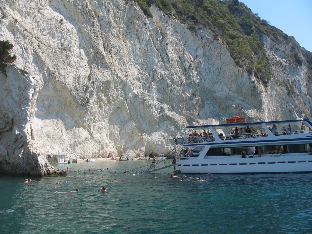 Ausflugsboot und Schwimmer vor der hellen Felswand der Insel Marathonisi in der Bucht von Laganas