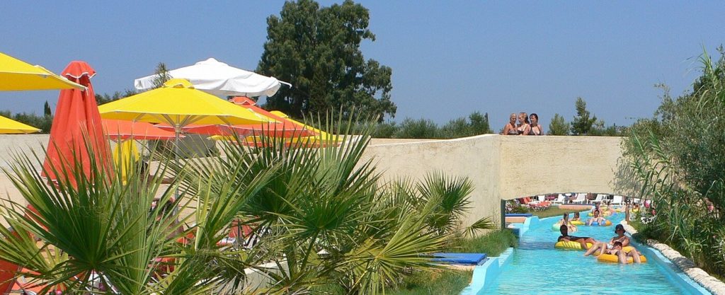 Langer Kanal mit türkisfarbenem Wasser zwischen Palmen, Sonnenschirmen und einer Mauer