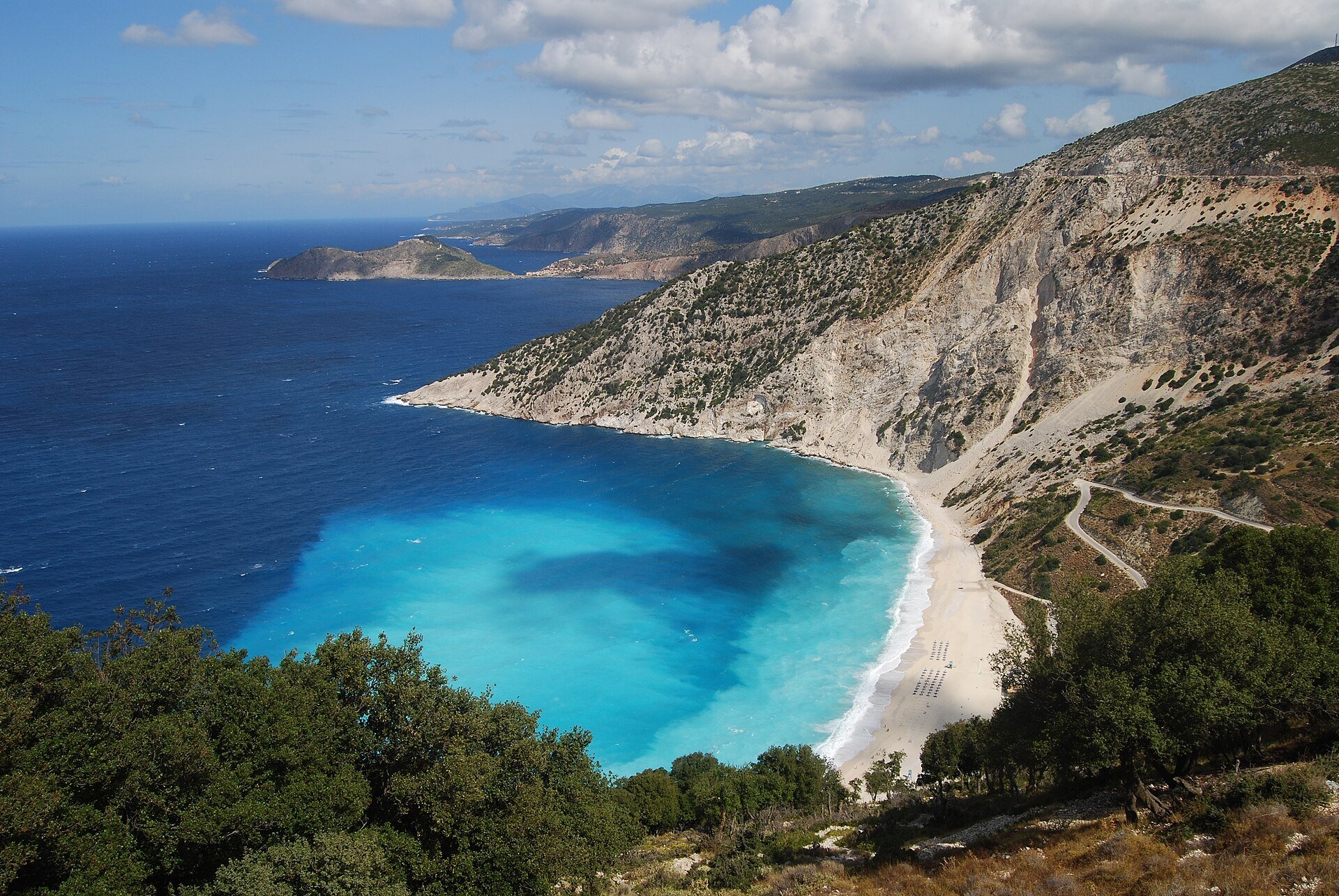 Blick von oben auf den weißen Strand von Myrtos unter hohen Hängen auf Kefalonia mit türkisfarbenem Wasser